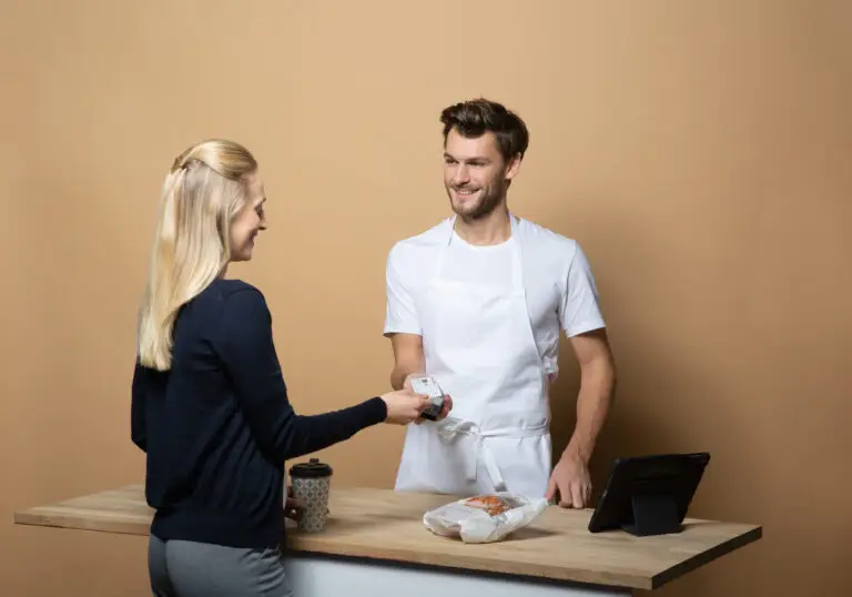 Kundin übergibt eine Zahlungskarte an einen freundlichen Verkäufer in einem Café, während ein Kaffeebecher auf der Theke steht.