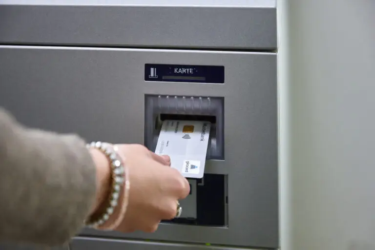 Hand, die eine Bankkarte in einen Geldautomaten einführt, mit dem Bildschirm, der die Aufforderung zur Karteneingabe anzeigt.