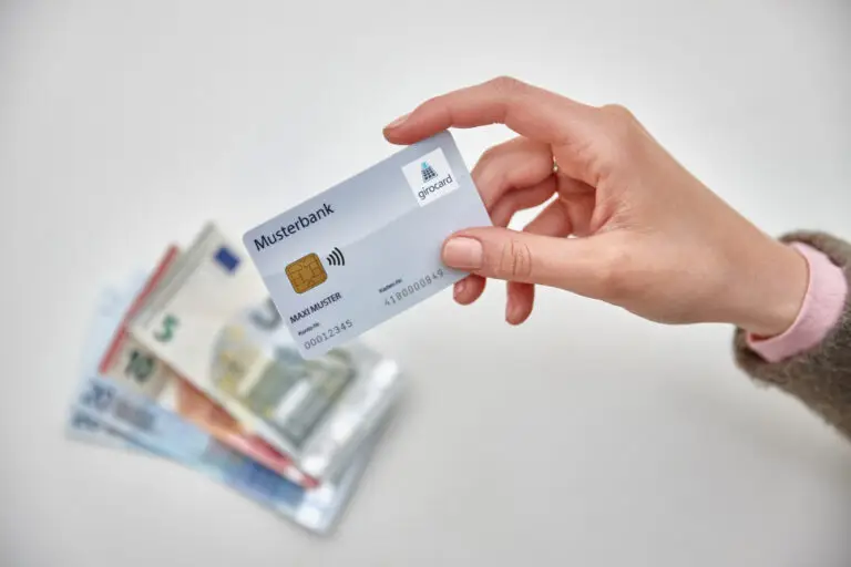 Hand hält eine girocard der Musterbank über einem Stapel Euro-Banknoten, symbolisiert moderne Zahlungsmethoden und finanzielle Transaktionen.