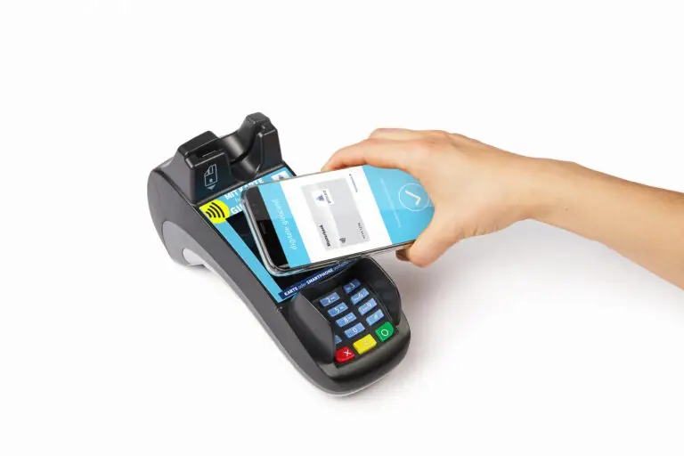 Hand mit Smartphone, die kontaktloses Bezahlen an einem Kartenlesegerät demonstriert, das für digitale Zahlungen geeignet ist.
