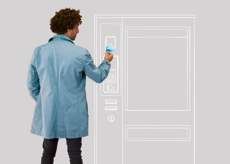 Mann im blauen Mantel nutzt ein kontaktloses Zahlungsmittel an einem Verkaufsautomaten vor einem grauen Hintergrund.