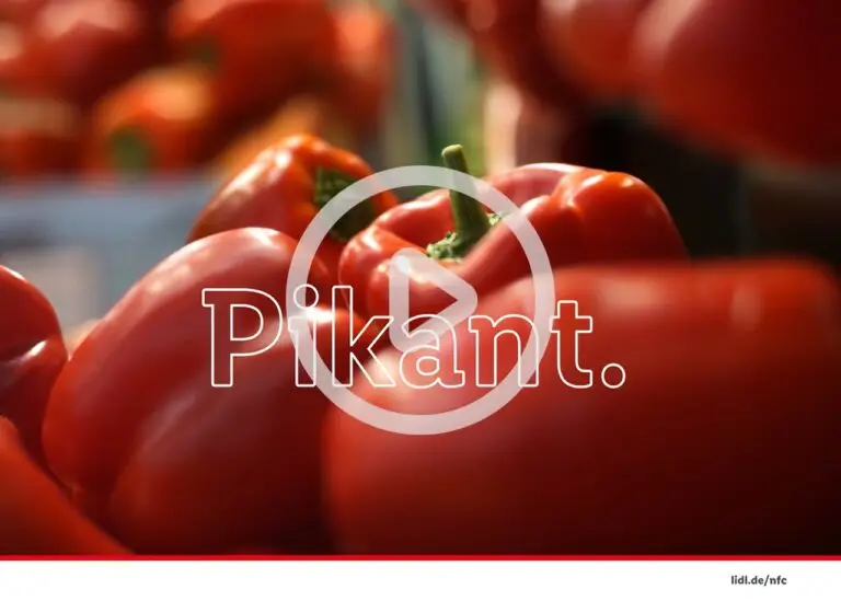 Nahaufnahme von frischen, roten Paprika, die in einem Markt präsentiert werden, mit dem Wort "Pikant" im Vordergrund, das auf den würzigen Geschmack hinweist.