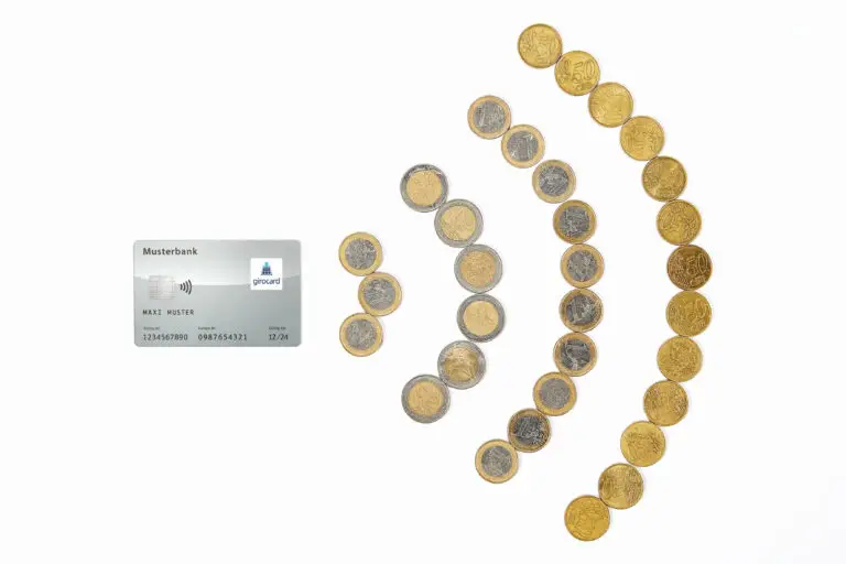 Bild einer Girokarte mit dem Logo einer Musterbank, umgeben von verschiedenen Münzen in Euro. Die Anordnung der Münzen zeigt eine Mischung aus 1-Euro-, 2-Euro- und 50-Cent-Münzen, die auf einem weißen Hintergrund platziert sind.