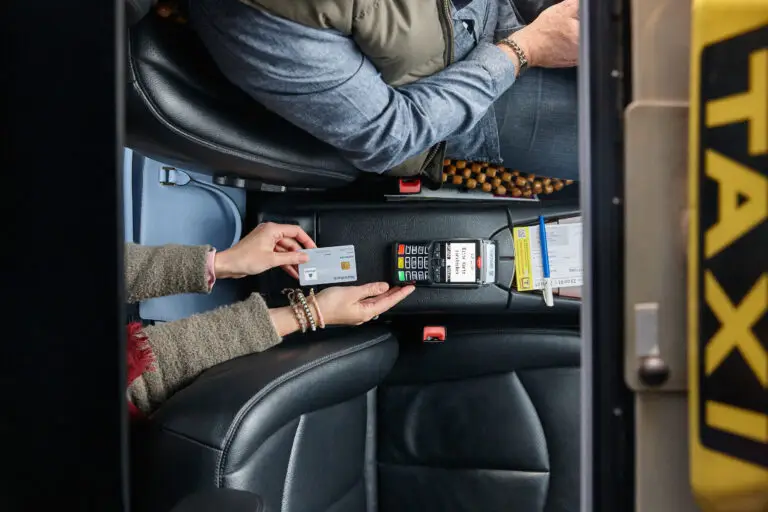 Zahlung mit Kreditkarte im Taxi, Hände halten eine Karte über das Kartenlesegerät, Fahrer sitzt auf der rechten Seite, Innenansicht des Fahrzeugs, modernes Zahlungsmittel.