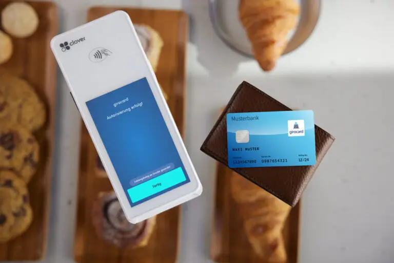 Mobile Zahlung mit girocard auf einem Clover-Terminal, das eine erfolgreiche Autorisierung anzeigt, während eine Bankkarte aus einem Geldbeutel gehalten wird, im Hintergrund Gebäck auf einem Holzbrett.