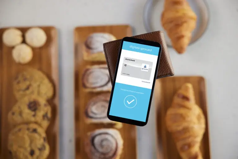 Smartphone mit digitaler Girocard-Anzeige in einer Brieftasche, umgeben von frisch gebackenem Gebäck auf Holzplatten, ideal für die Nutzung moderner Zahlungsmethoden in Cafés oder Bäckereien.