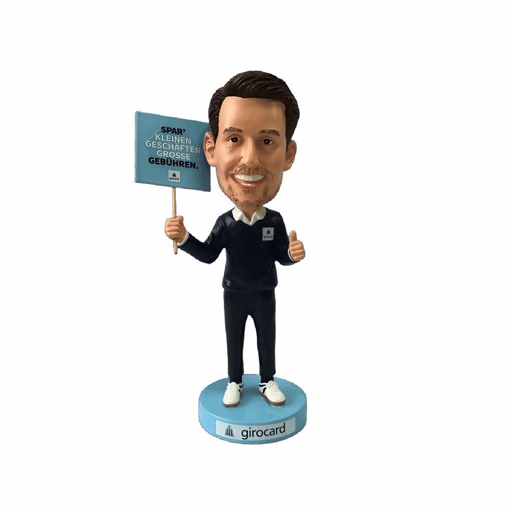 Bobblehead-Figur eines Mannes in einem dunkelblauen Outfit, der mit einem Daumen hoch zeigt und ein Schild mit der Aufschrift "SPAR' kleinen Geschäften große Gebühren" hält. Die Figur steht auf einem Sockel mit dem Schriftzug "girocard".