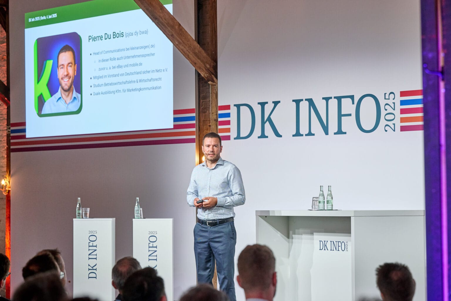 Pierre Du Bois präsentiert auf der DK INFO 2025, während im Hintergrund seine Informationen sowie beruflichen Stationen auf einer Leinwand angezeigt werden. Seine Rolle als Head of Communications bei kleinanzeigen.de wird hervorgehoben.