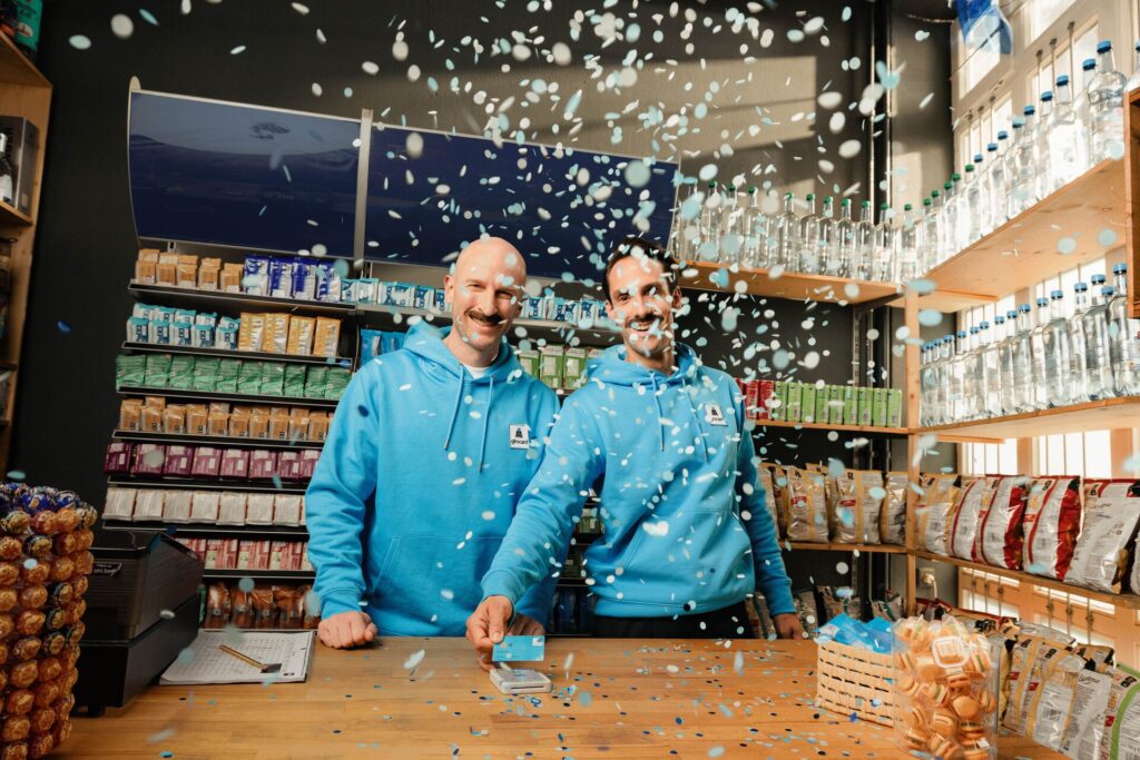 Zwei Mitarbeitende in girocard-Hoodies an der Ladenkasse, im Konfettiregen wird mit der girocard kontaktlos bezahlt