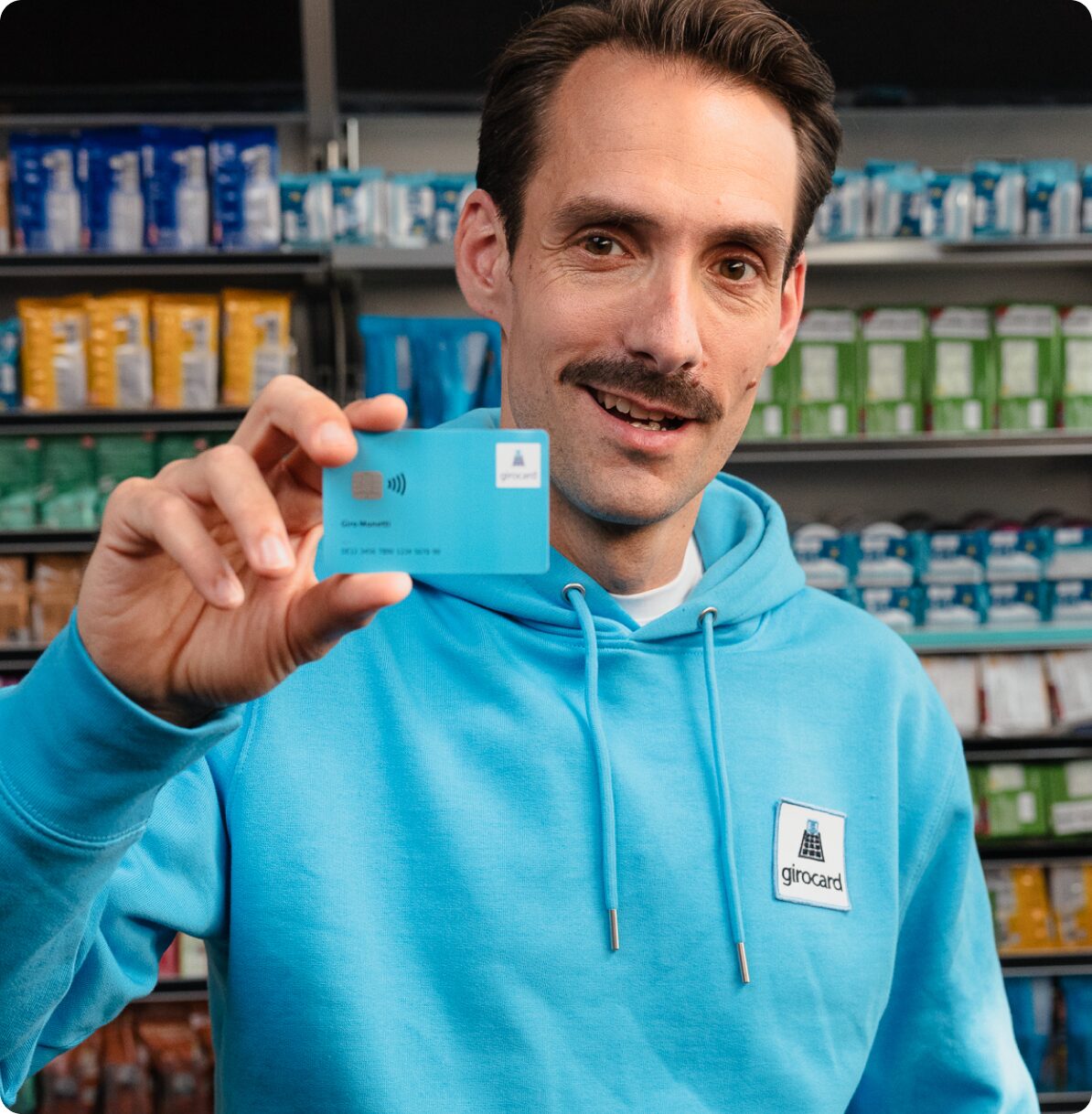 Mr. Giro hält im Laden eine girocard in die Kamera.