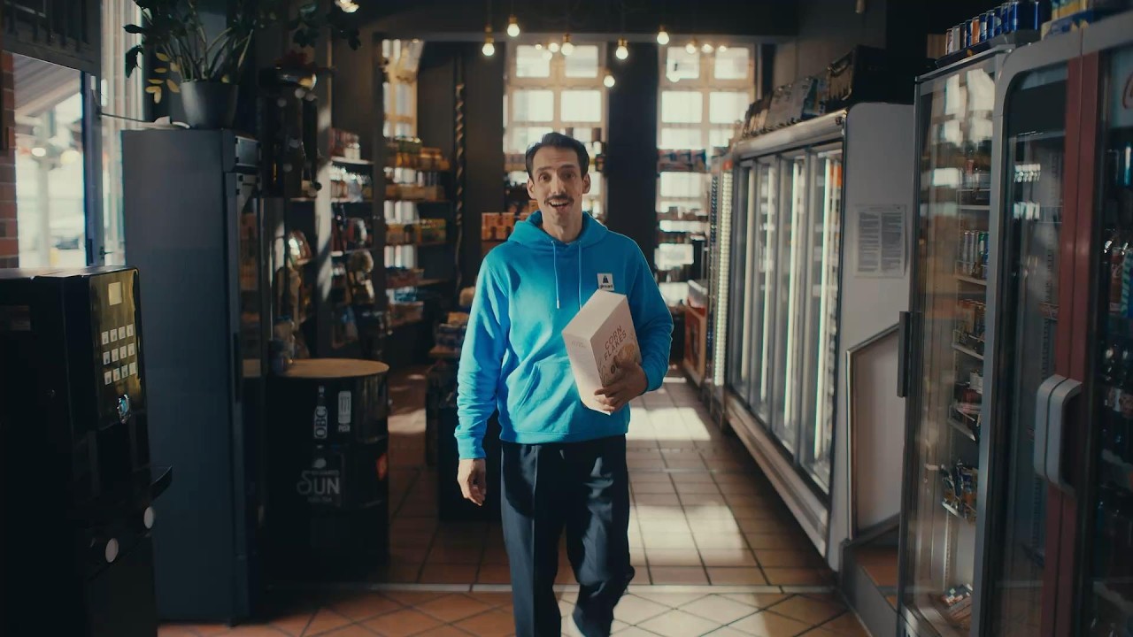 Mr. Giro im hellblauen girocard-Hoodie geht mit einer Papiertüte durch einen Getränkemarkt.