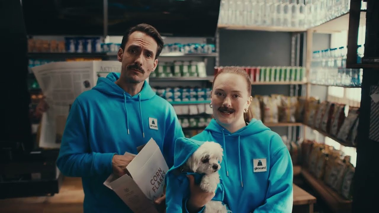 Mr. Giro mit einem Flyer neben einer Person, die einen kleinen weißen Hund im Arm hält.